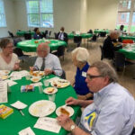 Gordon and fellow DCIA members at the DCIA annual banquet, post-COVID 19 shut down. Older white appearing men at a round table with a green table cloth, paper programs, and food in a large hall.